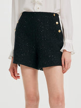 A lady wears black tweed shorts.